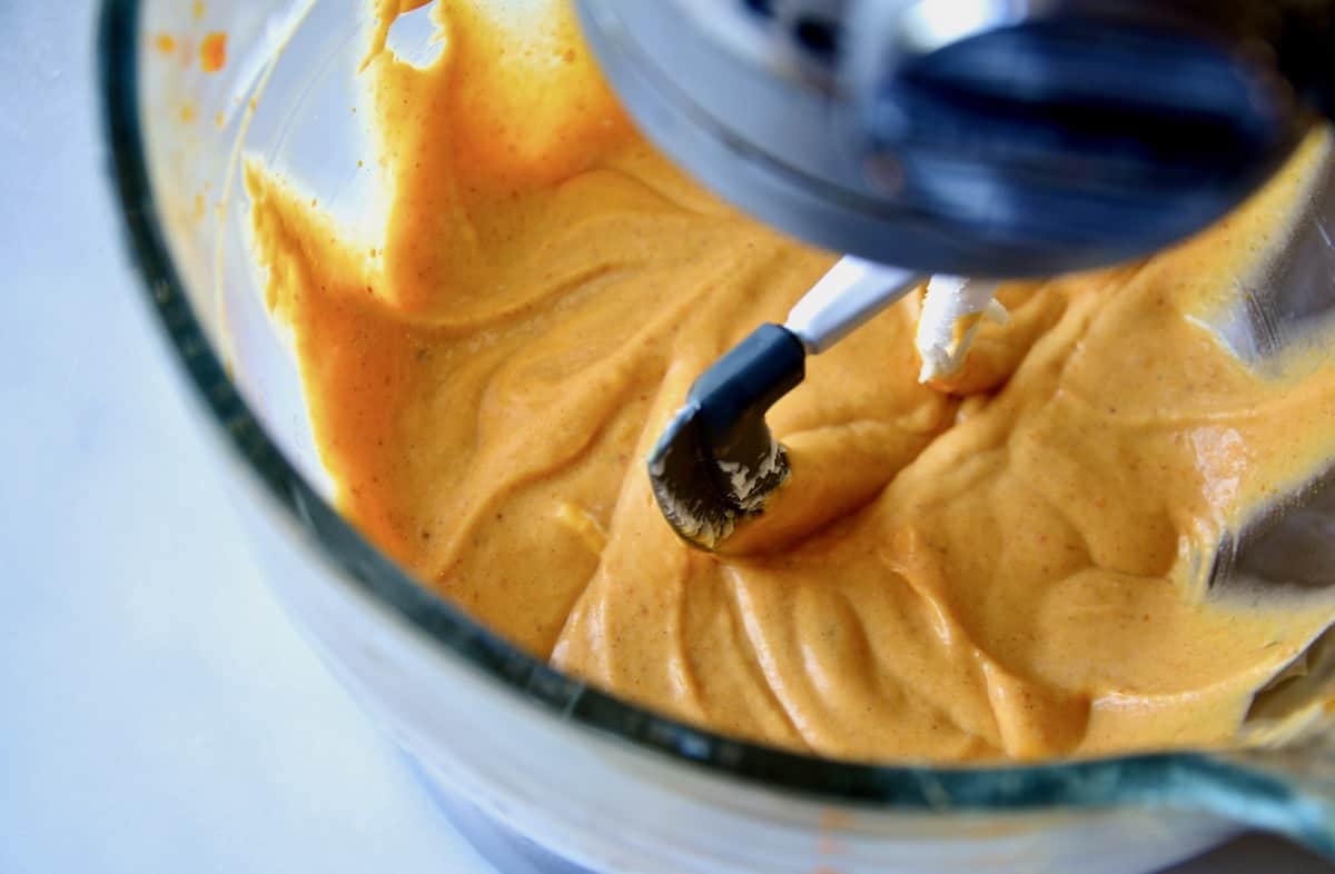 Pumpkin cheesecake batter in the bowl of a stand mixer fitted with a paddle attachment.