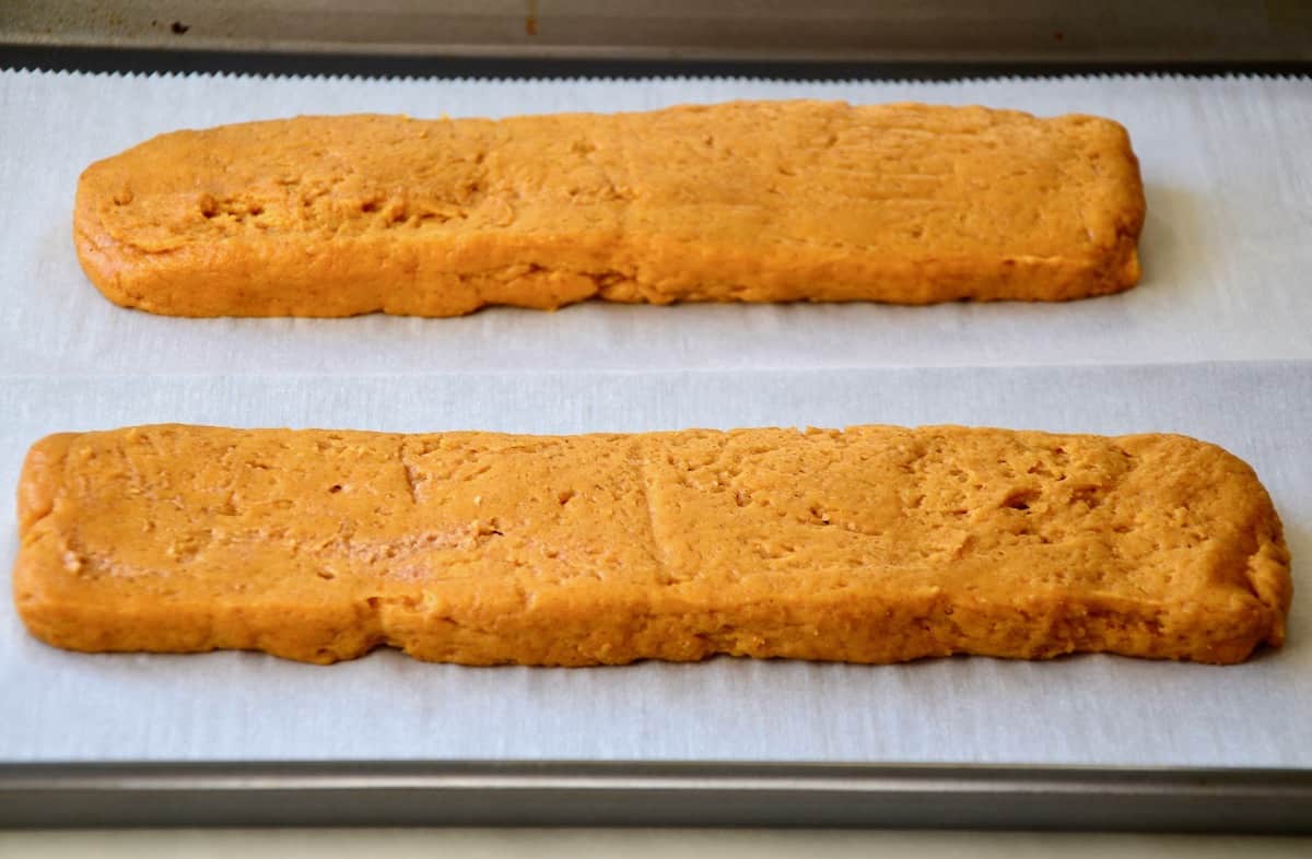 Two unbaked rectangles of pumpkin pie biscotti dough on a parchment-lined baking sheet.