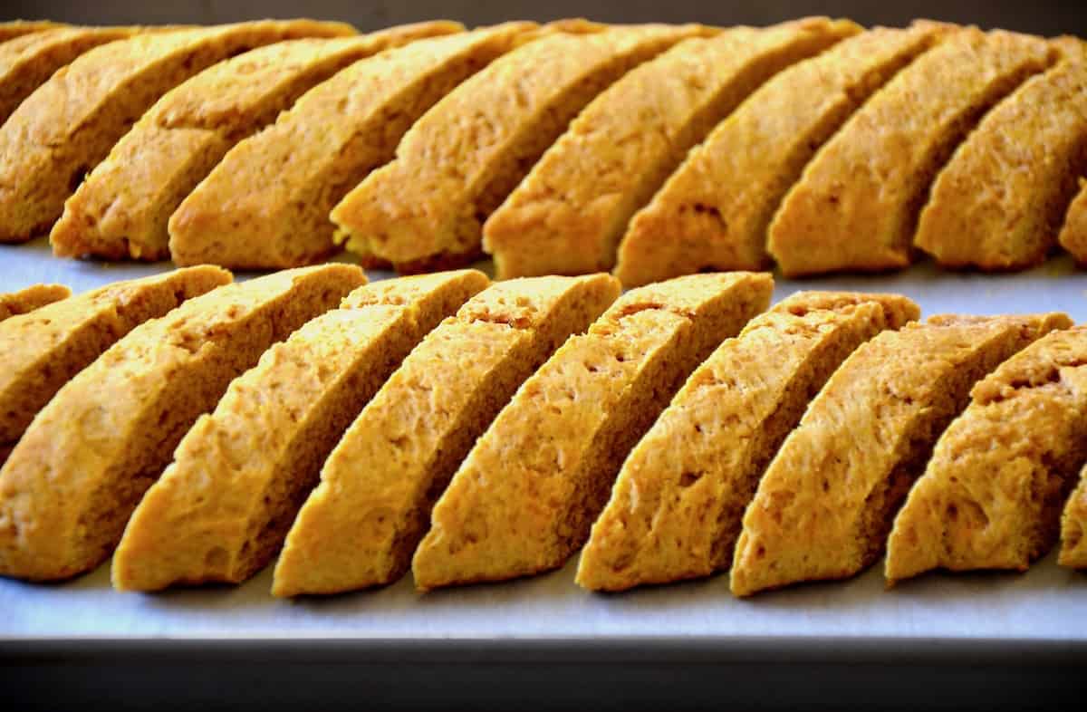 Two rows of sliced, baked pumpkin pie biscotti on a parchment-lined baking sheet.