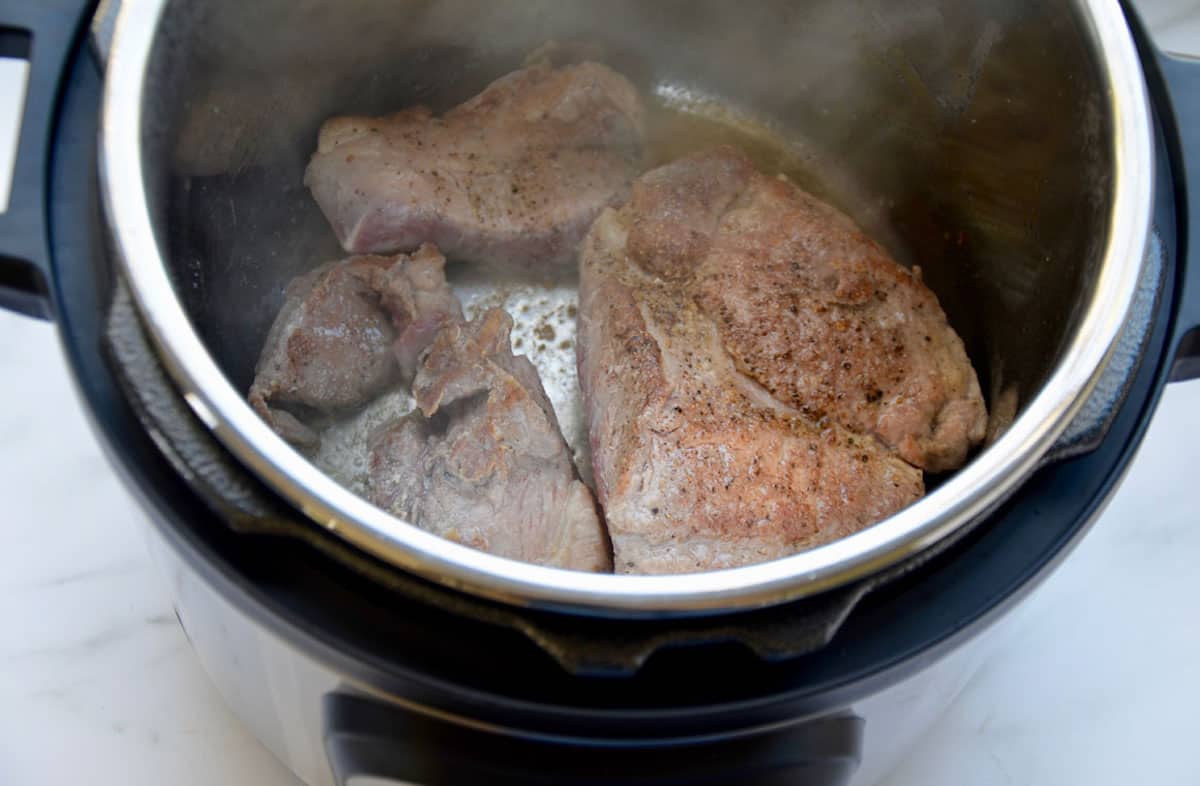 Three pieces of pork shoulder browning in an Instant Pot.