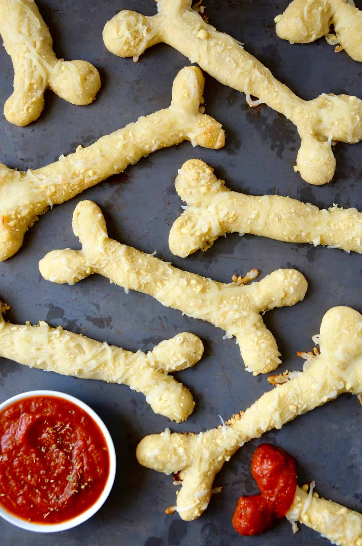 Several baked, cheesy breadstick bones with a small bowl of marinara sauce beside the breadsticks. An end of one of the breadsticks is dipped in marinara.