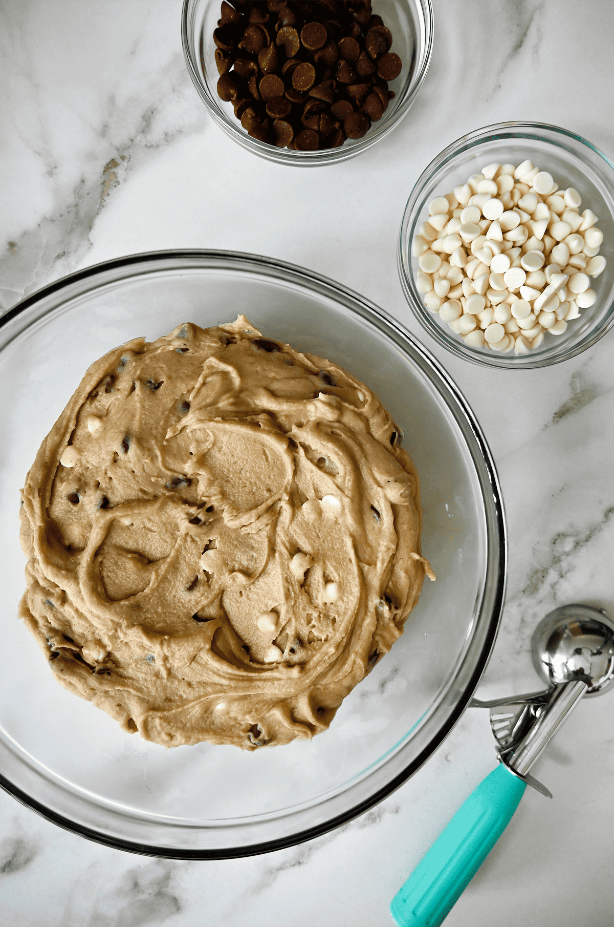 Chilled cookie dough in a glass bowl with two small bowls of chocolate chips next to it