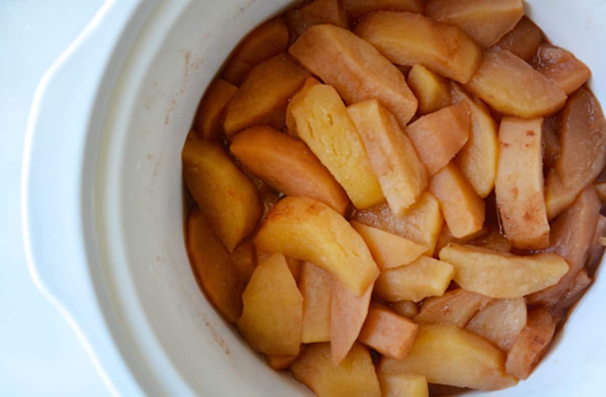 Cooked pieces of apple in the cooking pot of a slow cooker.