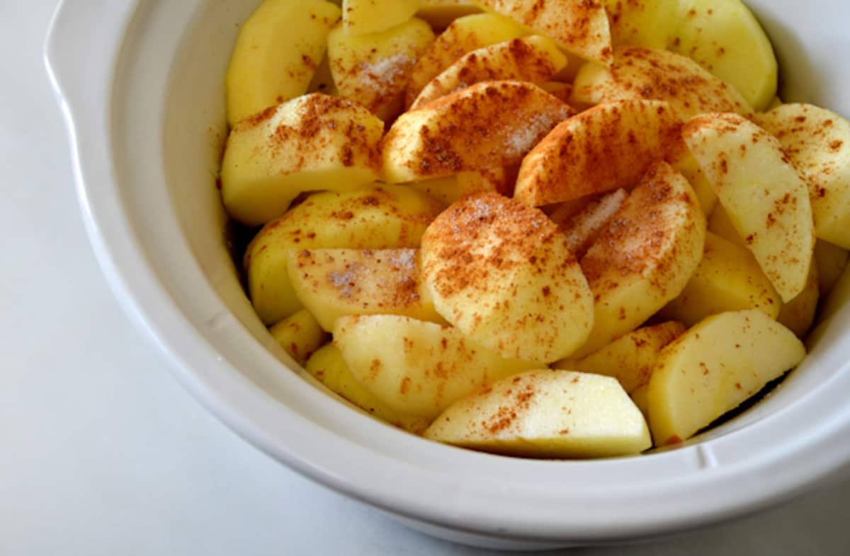 Pieces of raw apple with cinnamon and sugar on top in the cooking pot of a slow cooker.