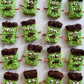 Four rows of Frankenstein Rice Krispie treats with candy eyes and pretzel stick bolts.