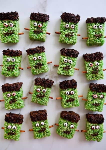 Four rows of Frankenstein Rice Krispie treats with candy eyes and pretzel stick bolts.