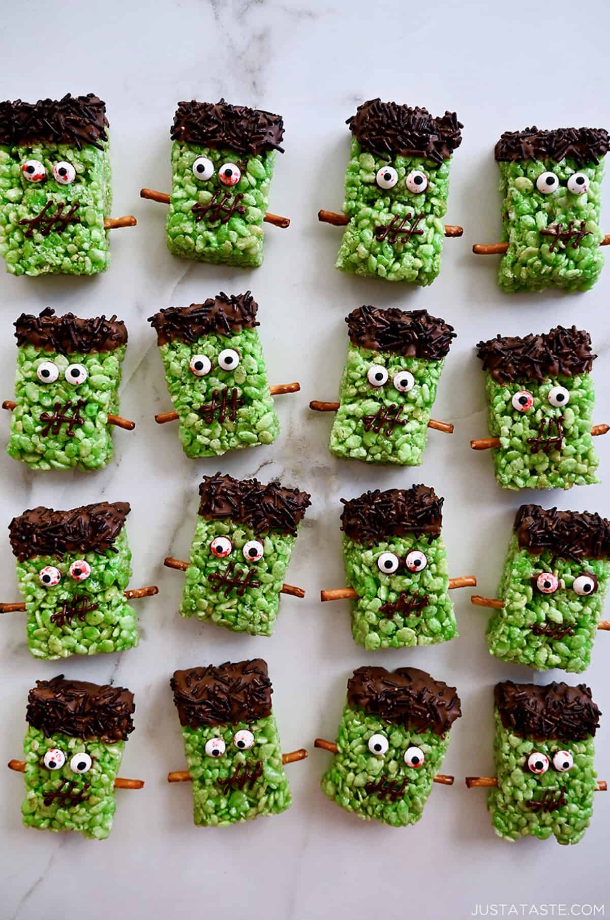 Four rows of Frankenstein Rice Krispie treats with candy eyes and pretzel stick bolts.
