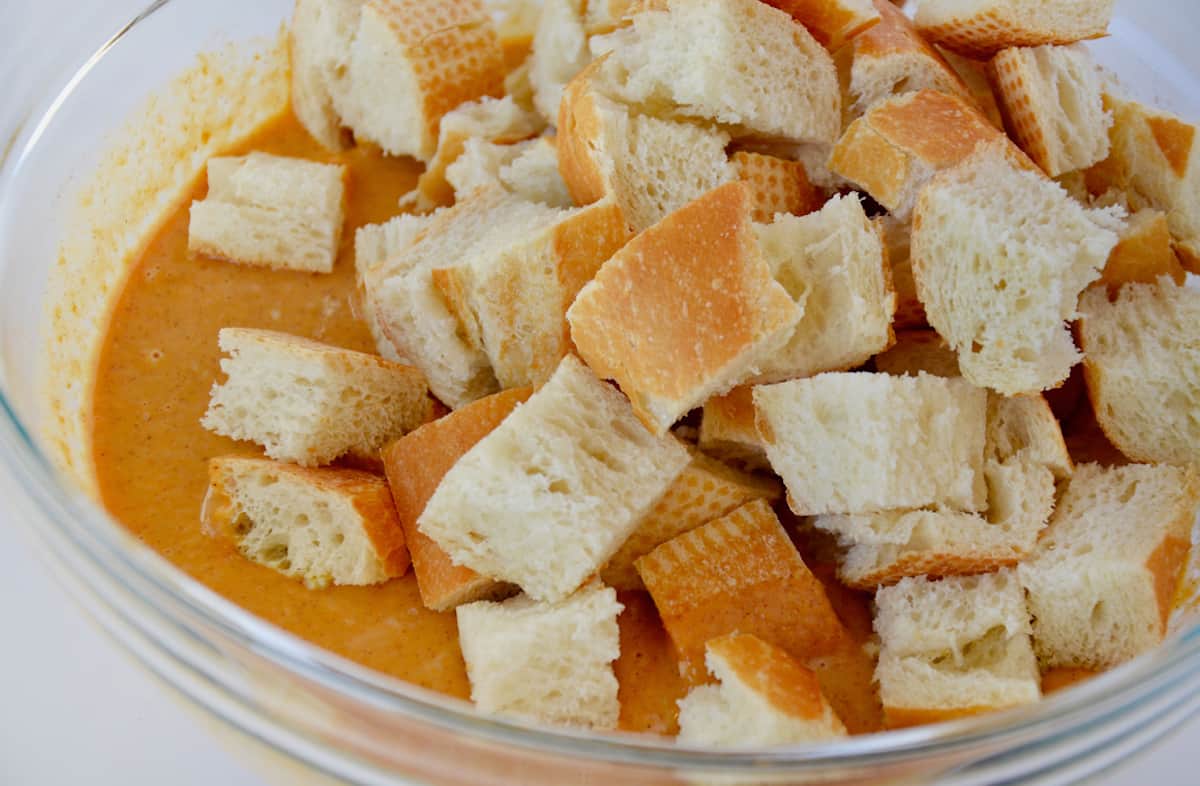 Cubes of bread and pumpkin custard in a glass mixing bowl.