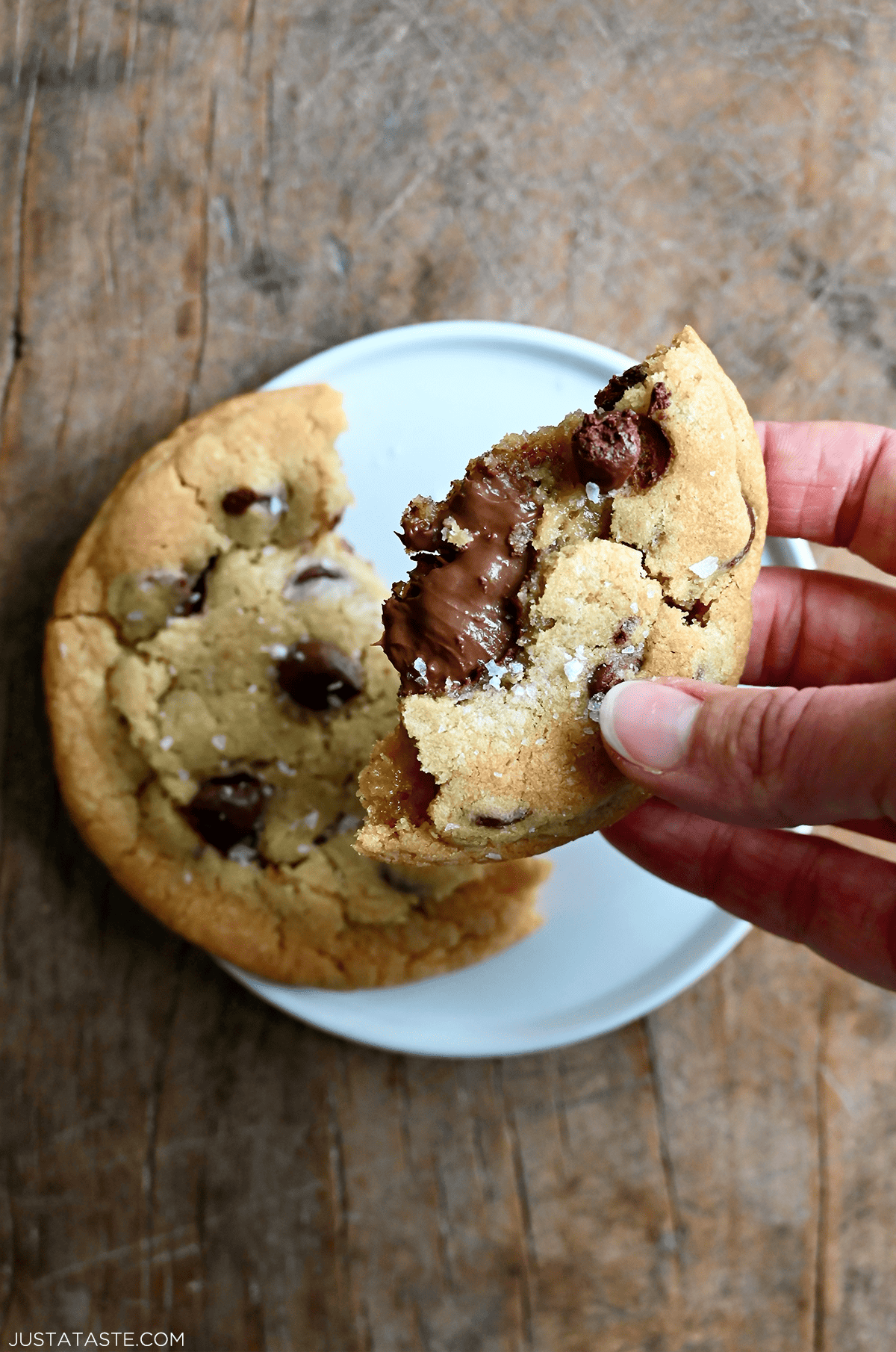 A hand holds half of a chocolate chip cookie with a gooey Nutella filling.