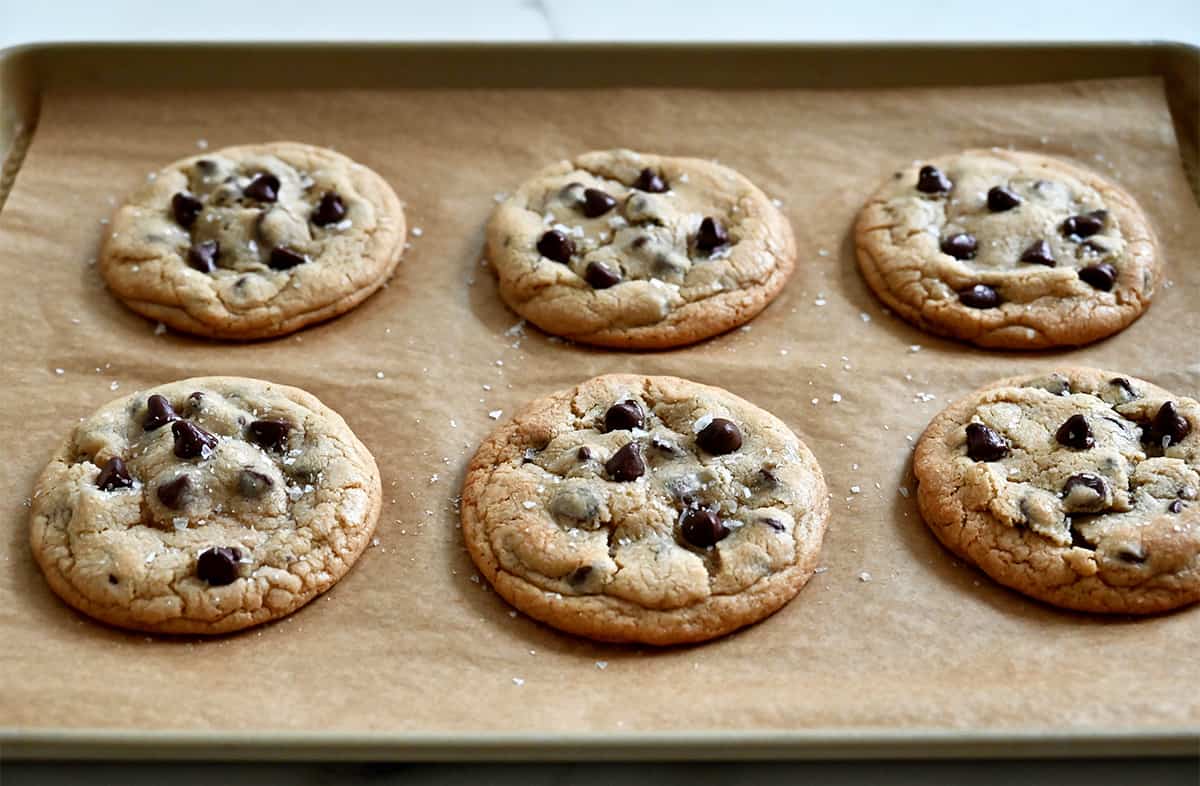 Stuffed cookies with chocolate chips sprinkled with large-flake sea salt cooling on a parchment paper-lined baking sheet.