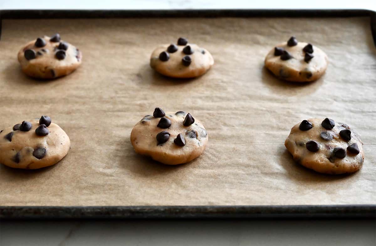 Cookie dough balls topped with chocolate chips on a baking sheet lined with parchment paper.