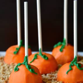 Pumpkin cheesecake pops sitting on graham cracker crumbs on a white serving platter.