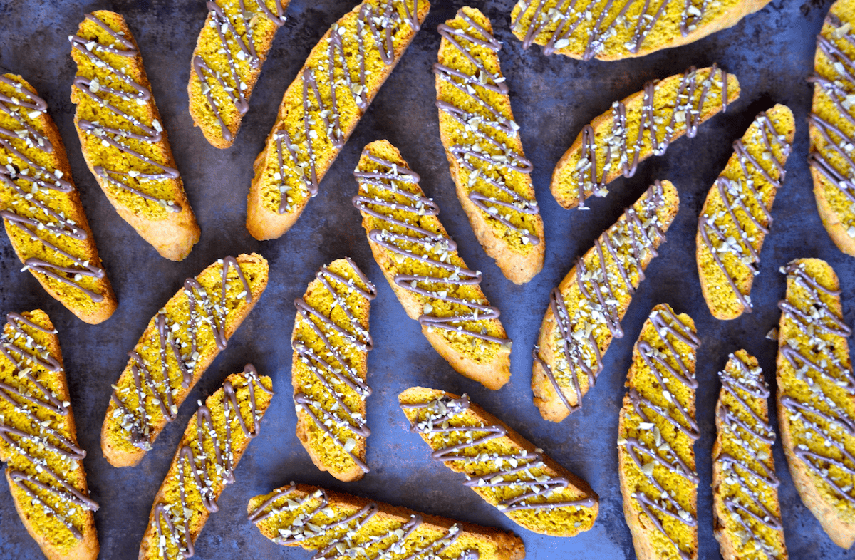 A number of pumpkin pie biscotti that are drizzled with melted chocolate and topped with chopped pumpkin seeds.