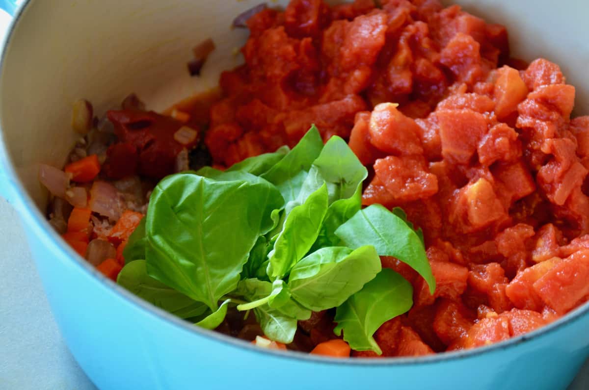 Canned San Marzano tomatoes and a sprig of fresh basil are added to a light-blue Dutch oven.