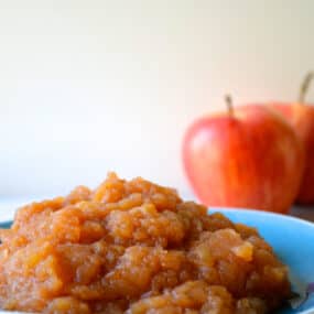 A bowl of slow cooker applesauce. Two apples are stationed behind the bowl.