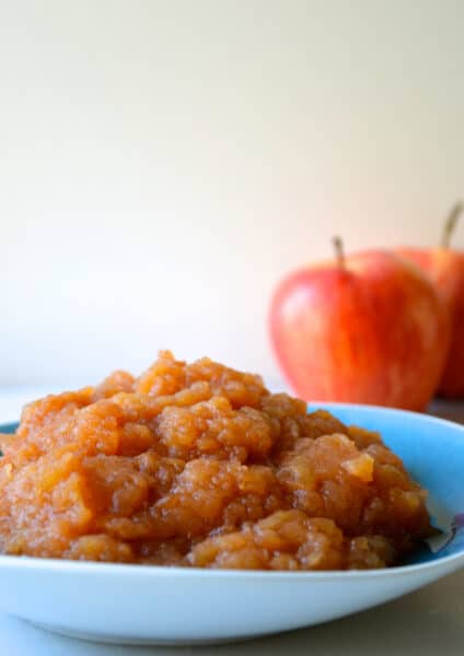 A bowl of slow cooker applesauce. Two apples are stationed behind the bowl.