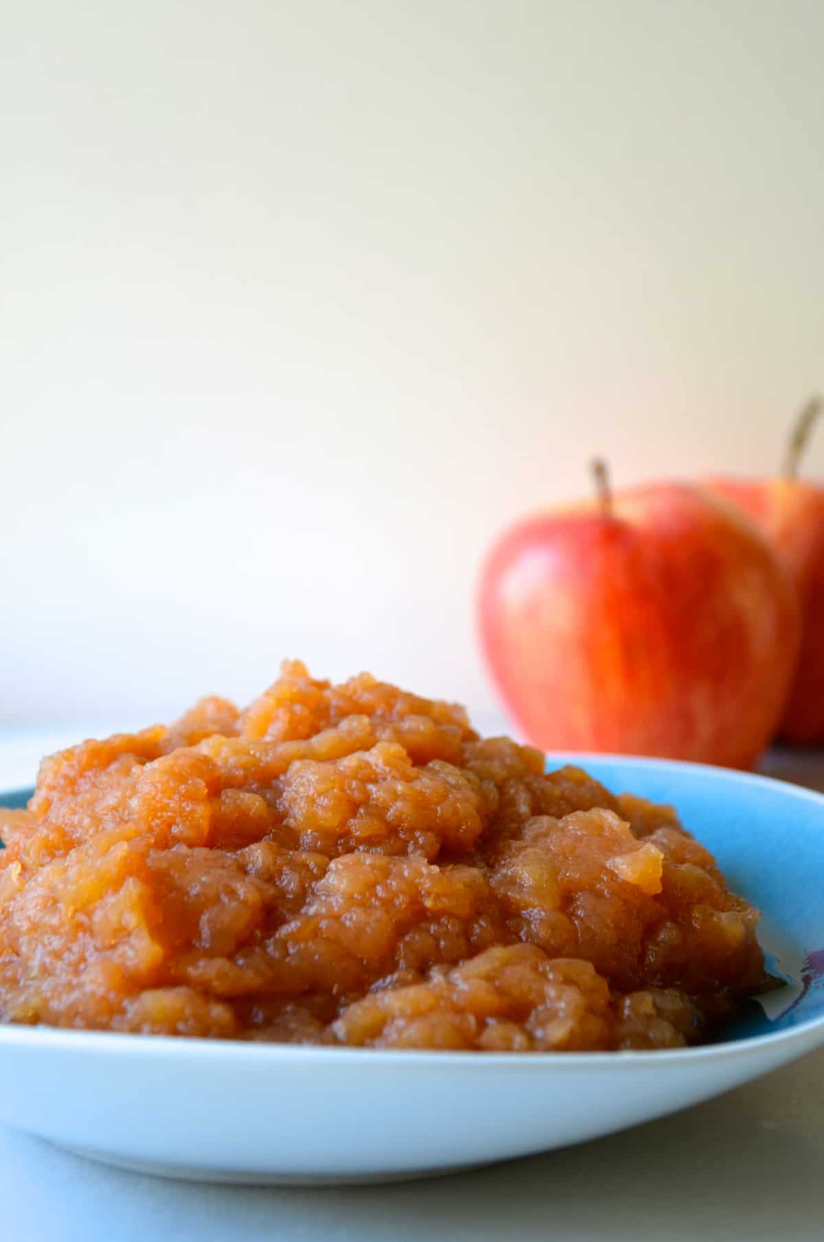 A bowl containing applesauce. Two apples are stationed behind the bowl.