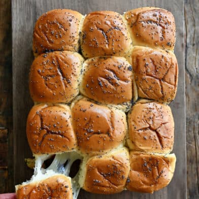 A hand pulls a turkey slider apart from other sliders on a cutting board.