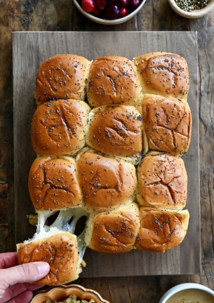 A hand pulls a turkey slider apart from other sliders on a cutting board.