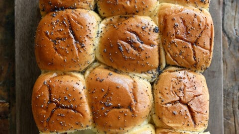 A hand pulls a turkey slider apart from other sliders on a cutting board.