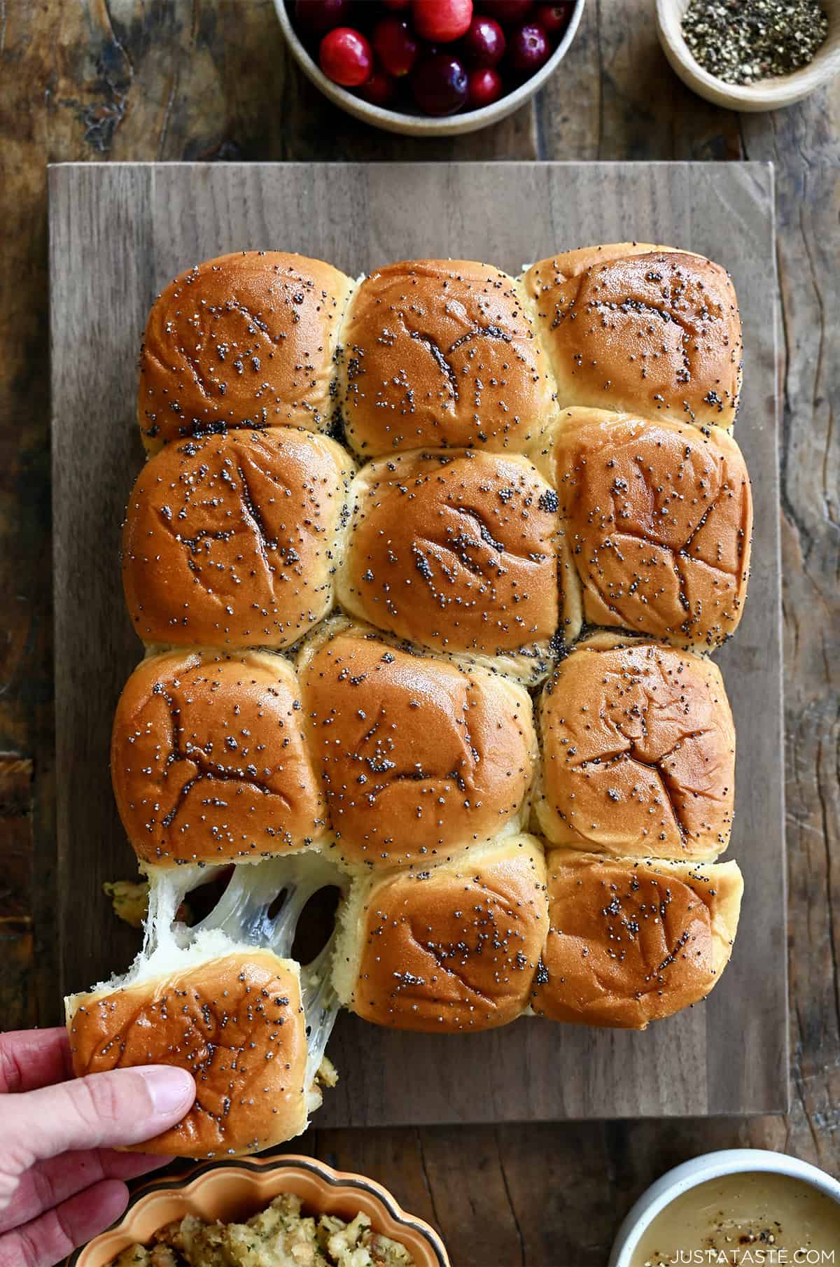 A hand pulls a turkey slider apart from other sliders on a cutting board.