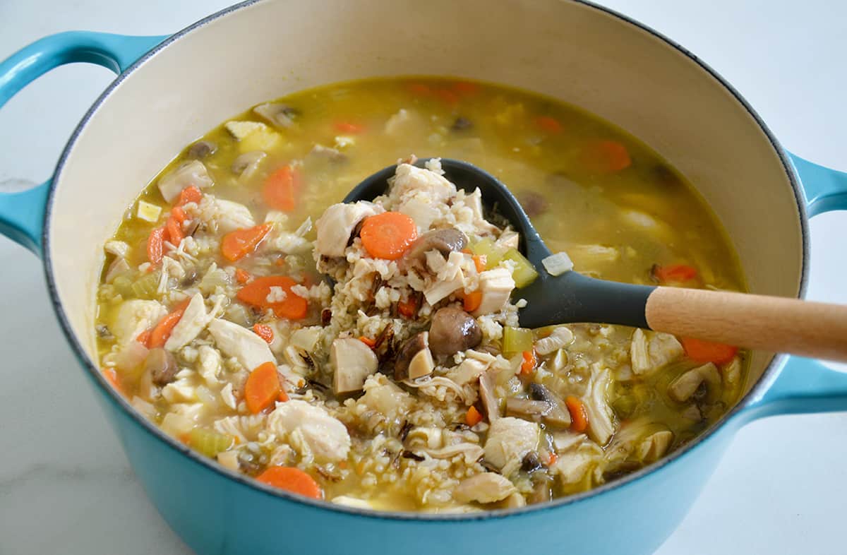 A ladle scooping chicken wild rice soup out of a Dutch oven.