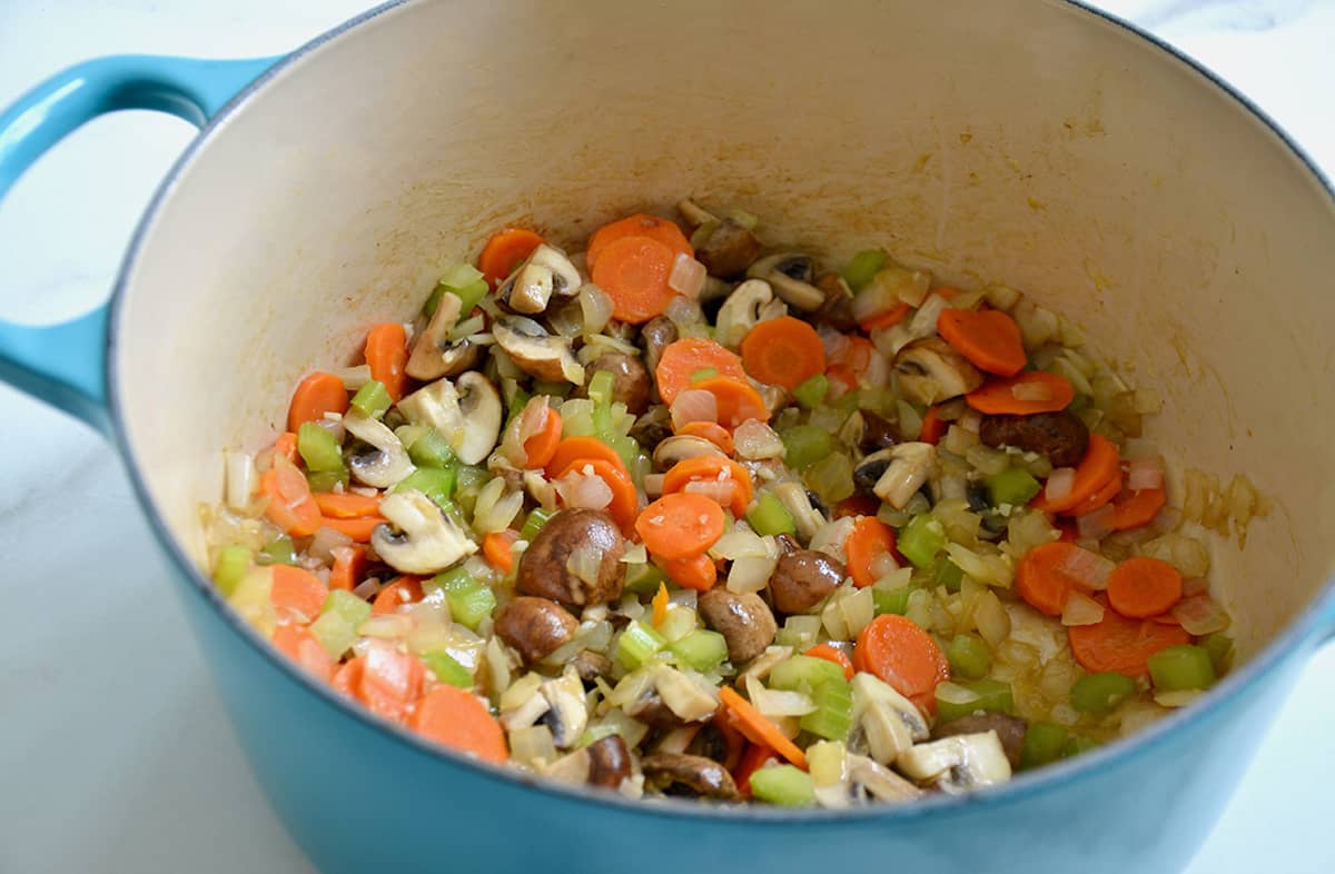 A mixture of chopped onions, carrots, celery, garlic and mushrooms in a blue Dutch oven.