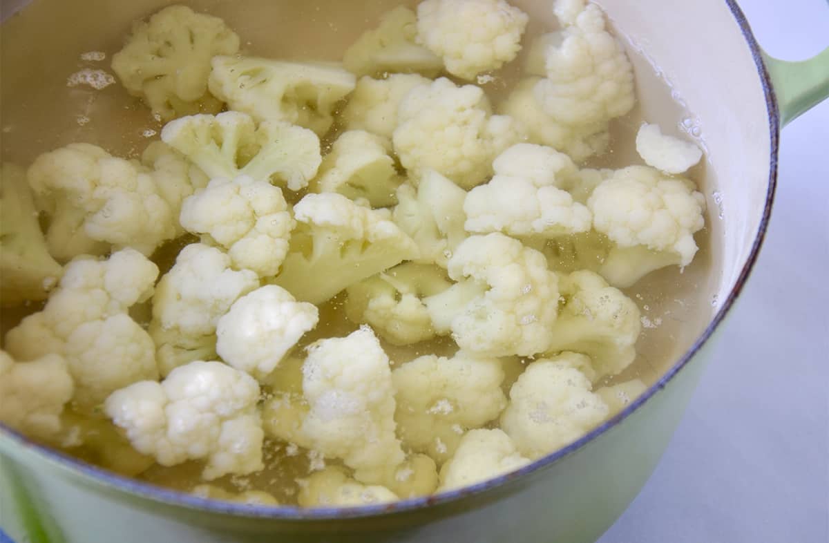 Cauliflower florets submerged in water in a Dutch oven.