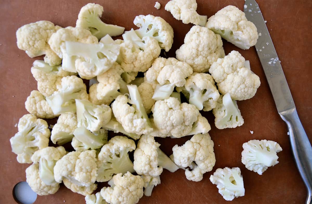 Cauliflower florets on a cutting board. A knife is beside the florets.