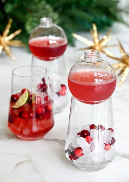 Three cocktail glasses containing ice, fresh cranberries and cranberry margarita mix.