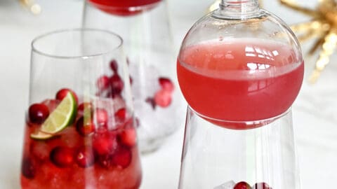 Three cocktail glasses containing ice, fresh cranberries and cranberry margarita mix.
