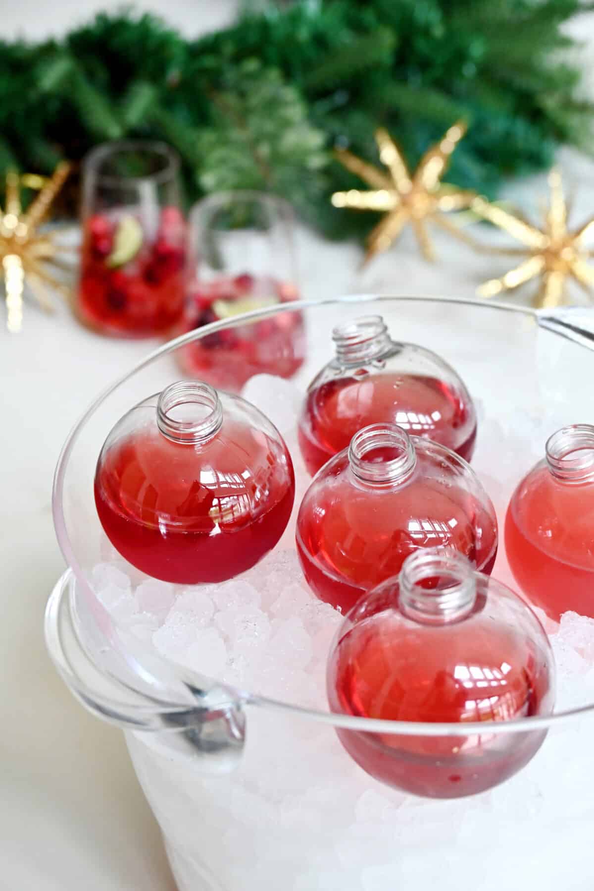 Clear ornament drinking balls filled with cranberry margaritas nestled in ice in a clear ice bucket.