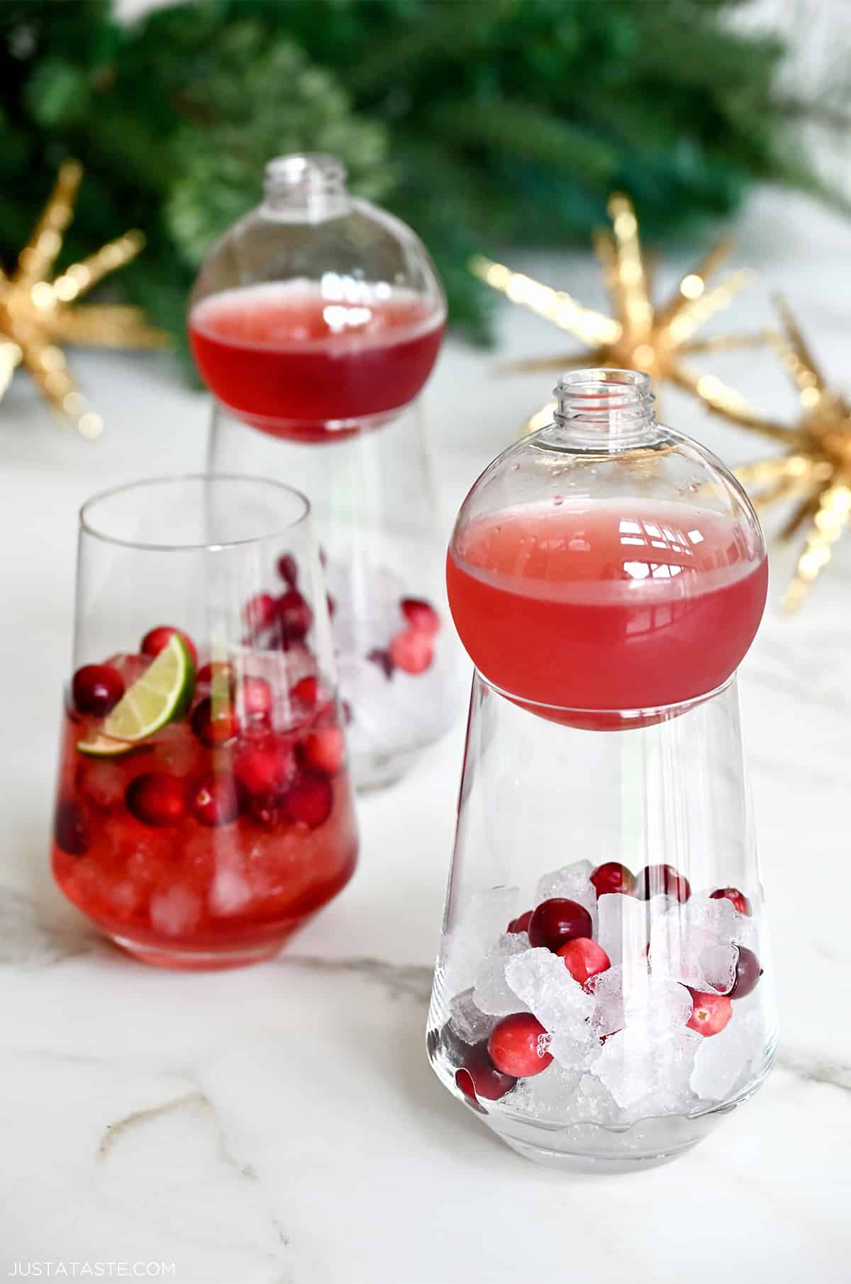 Three cocktail glasses containing ice, fresh cranberries and cranberry margarita mix.