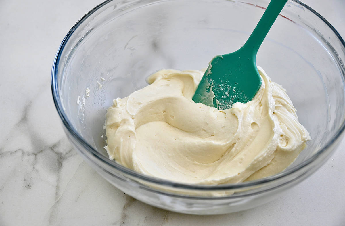 Cream cheese frosting in a glass mixing bowl. A spatula rests against the side of the bowl.