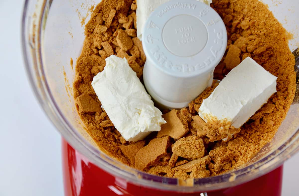 Cream cheese and gingersnap cookie crumbs in the bowl of a food processor.