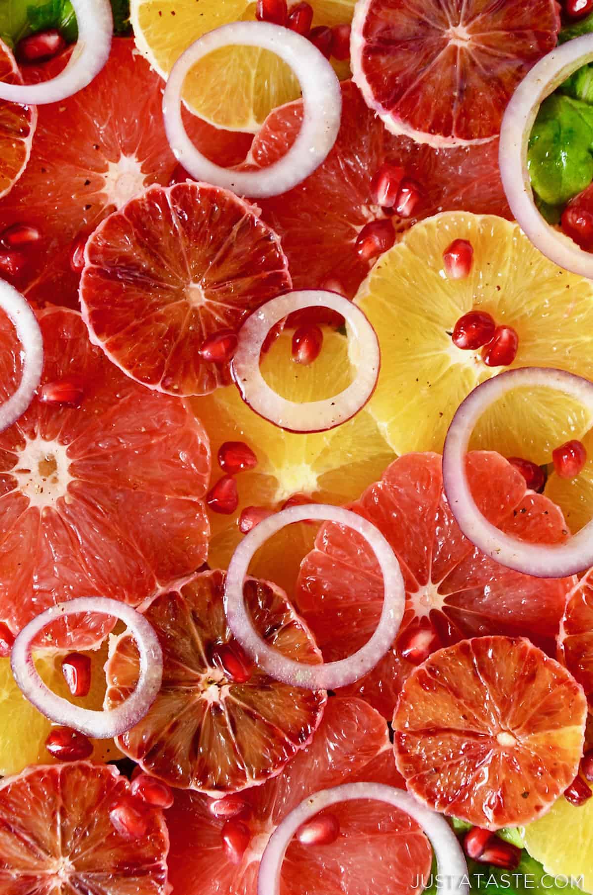 A salad made up of layers of sliced oranges, blood oranges and grapefruits, red onion slices, arugula and pomegranate seeds.