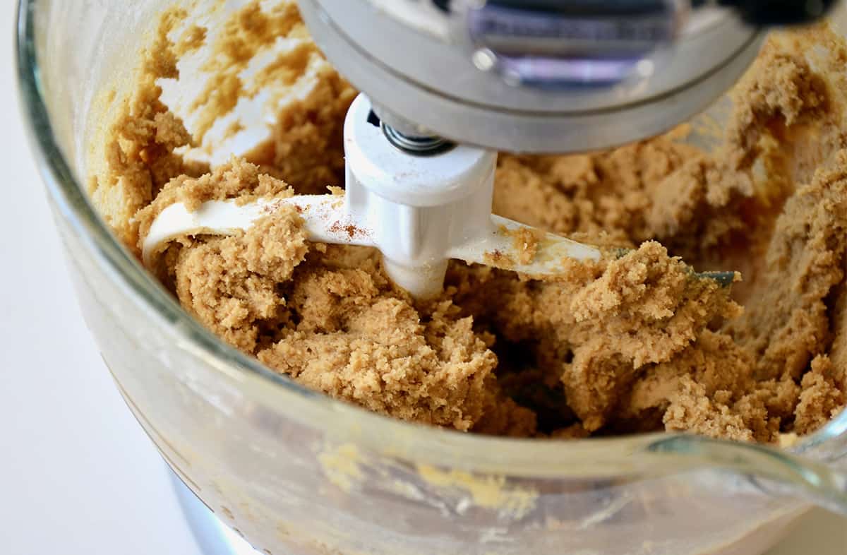 Gingerbread cookie dough in the bowl of stand mixer fitted with a paddle attachment.