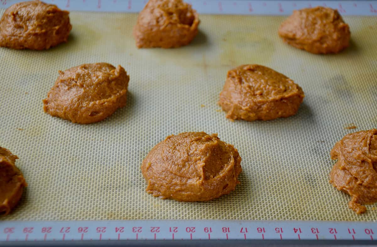 Portions of pumpkin whoopie pie batter evenly spaced apart on a Silpat-lined baking sheet.