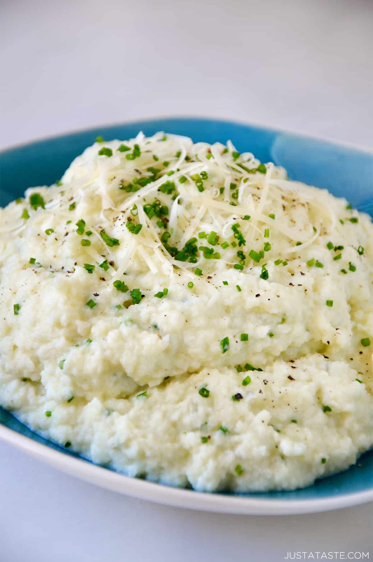 Mashed cauliflower topped with grated cheese, minced chives and black pepper in a bowl.