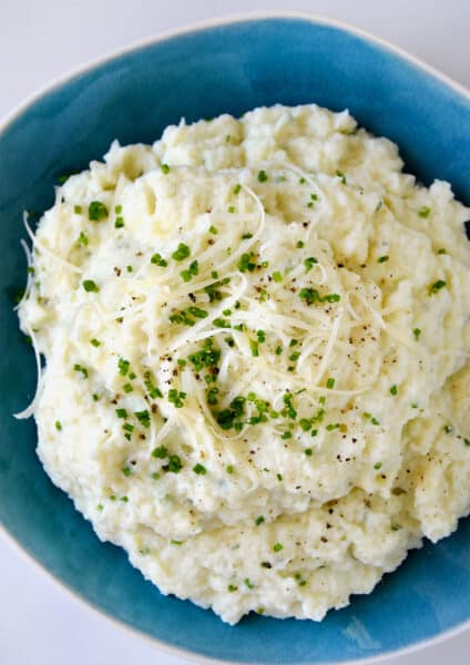 Mashed cauliflower topped with shredded cheese, finely minced chives and black pepper in a blue bowl.