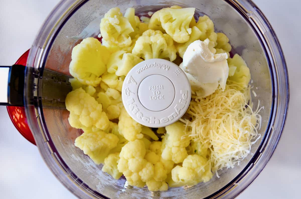 Cauliflower florets, grated cheese and cream cheese in the bowl of a food processor.