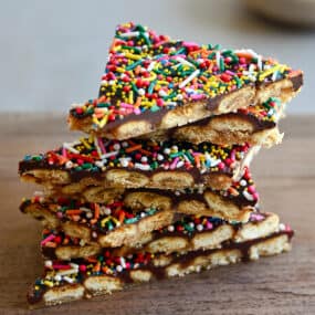 A stack of oyster cracker toffee bark with rainbow sprinkles on a wood cutting board.