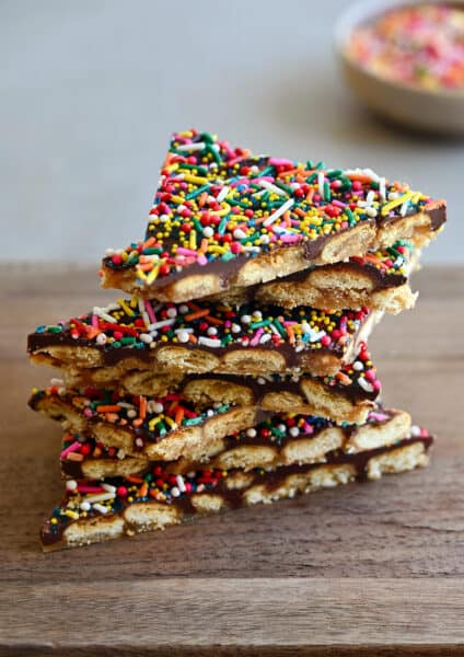 A stack of oyster cracker toffee bark with rainbow sprinkles on a wood cutting board.