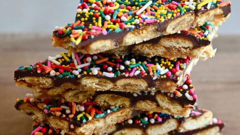 A stack of oyster cracker toffee bark with rainbow sprinkles on a wood cutting board.