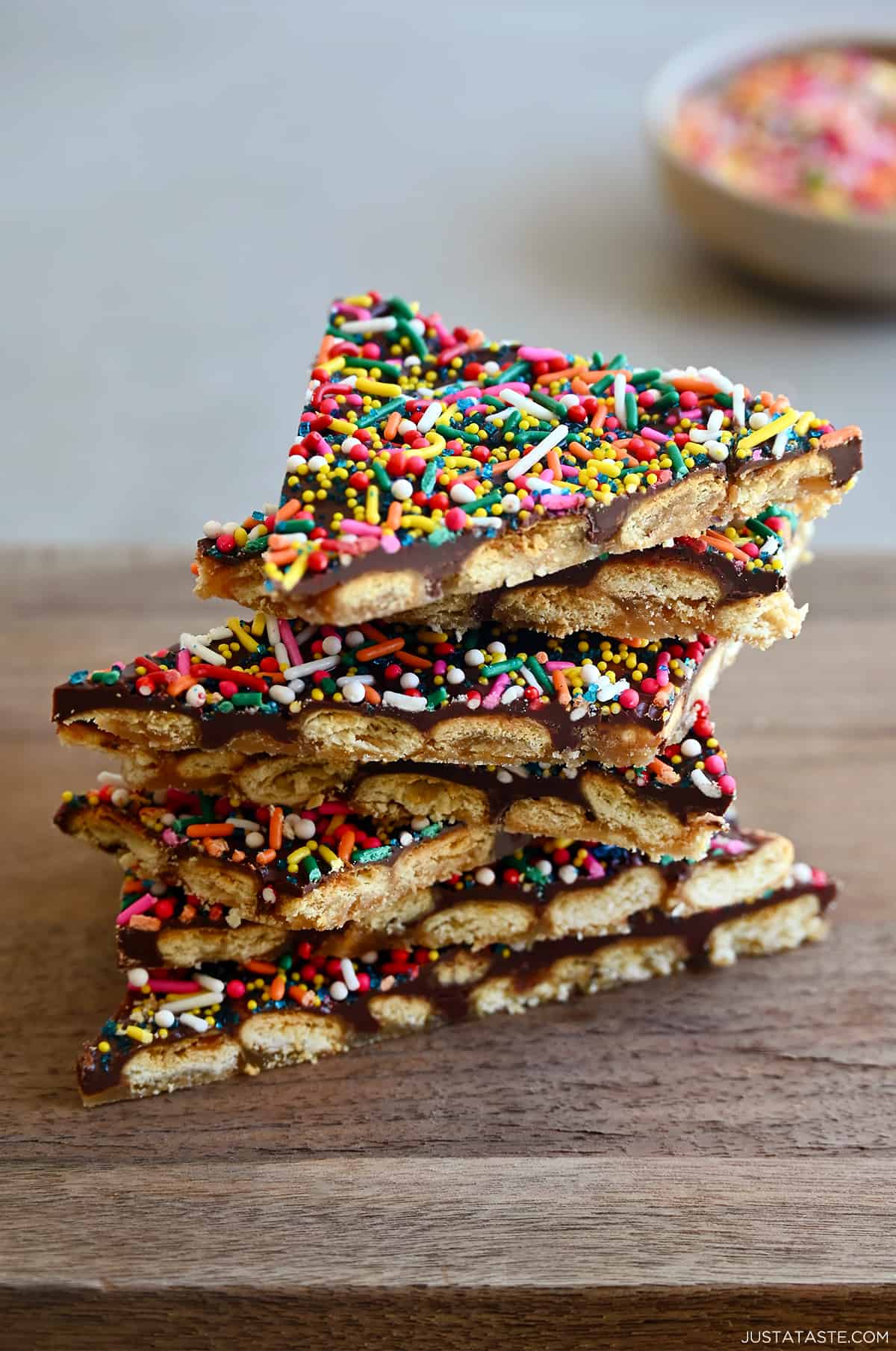 A stack of oyster cracker toffee bark with rainbow sprinkles on a wood cutting board.