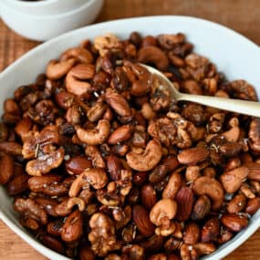 A bowl of roasted nuts with a spoon in it. A small bowl containing some more nuts and another holding salt sit behind it.