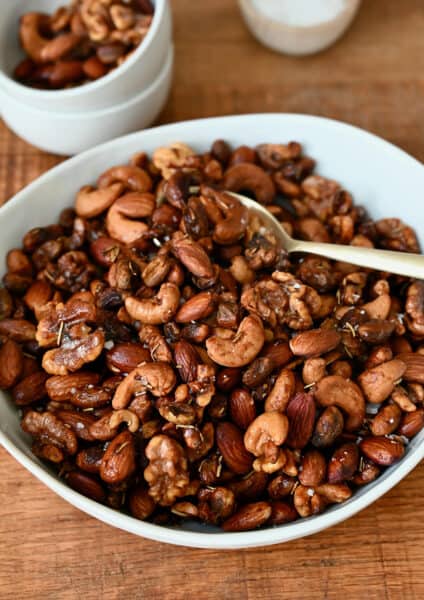 A bowl of roasted nuts with a spoon in it. A small bowl containing some more nuts and another holding salt sit behind it.