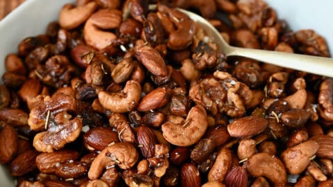 A bowl of roasted nuts with a spoon in it. A small bowl containing some more nuts and another holding salt sit behind it.