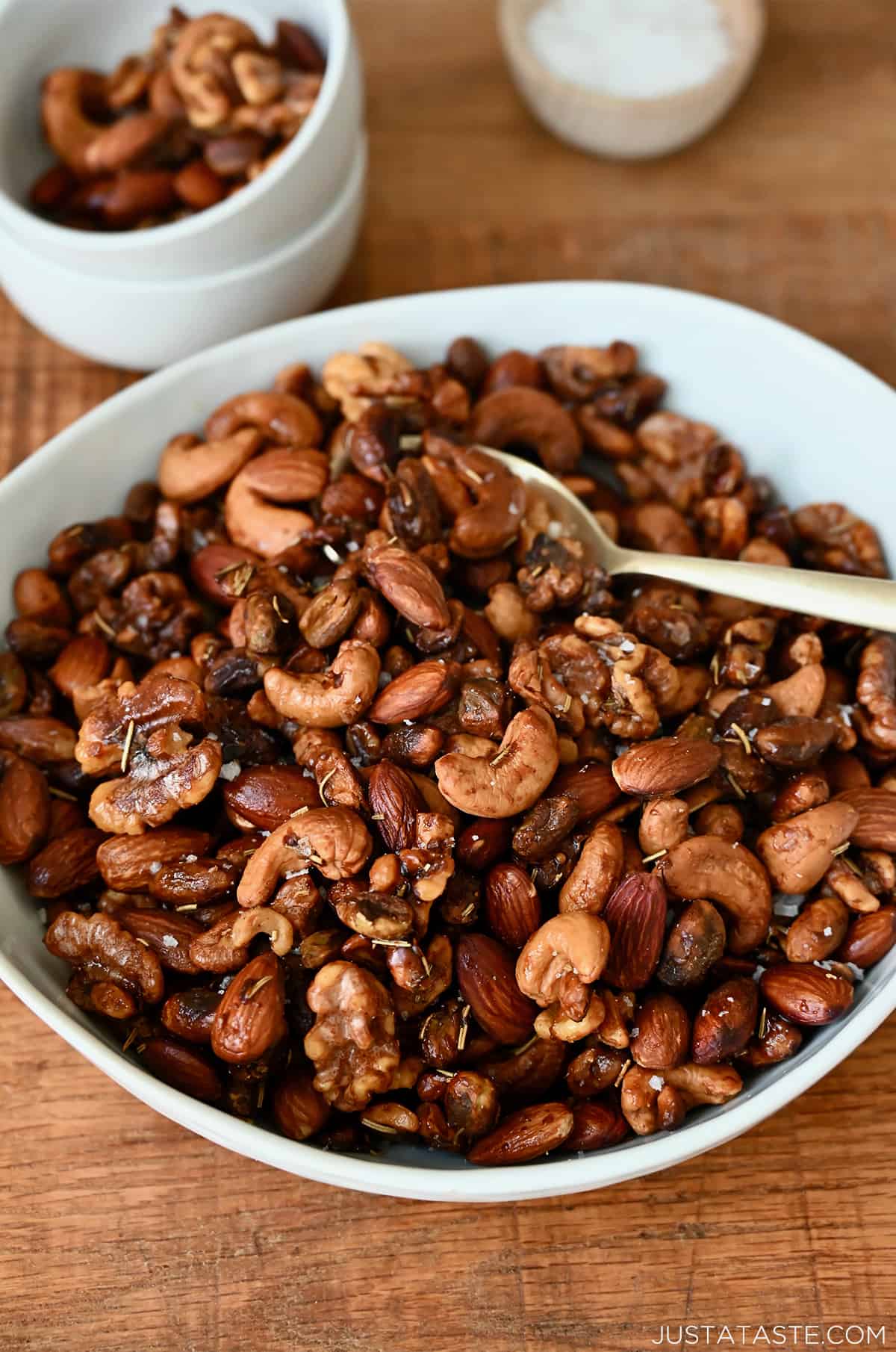 A bowl of roasted nuts with a spoon in it. A small bowl containing some more nuts and another holding salt sit behind it.