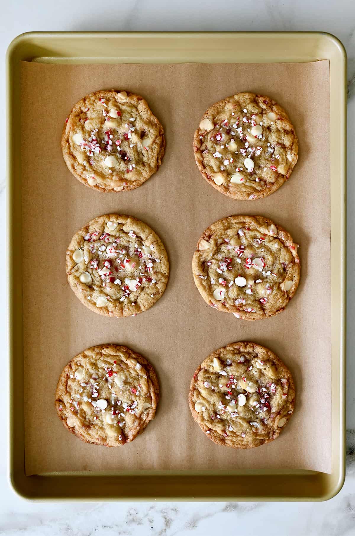 Six peppermint white chocolate chip cookies cooling on a parchment paper-lined baking sheet.